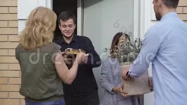 年轻幸福的一家人站在门口等着邻居给他们送蛋糕和一桶花